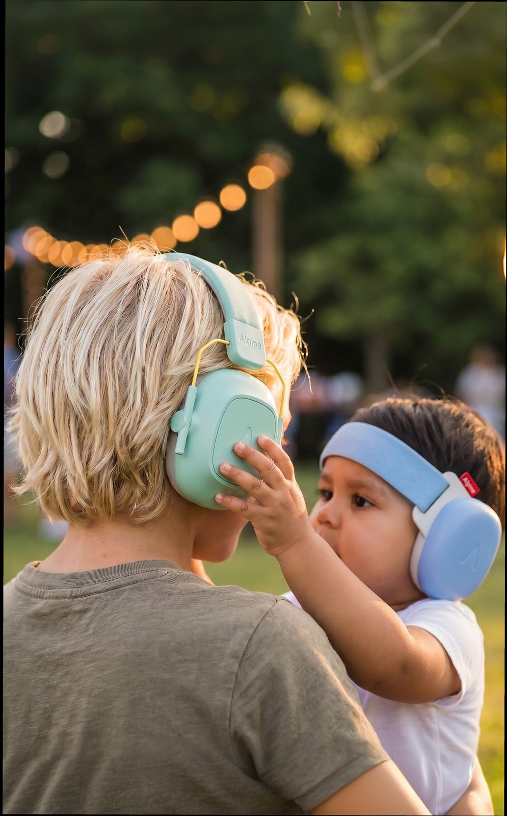 Baby in blue Muffy earmuffs reaching for a toddler's mint earmuffs at a garden party